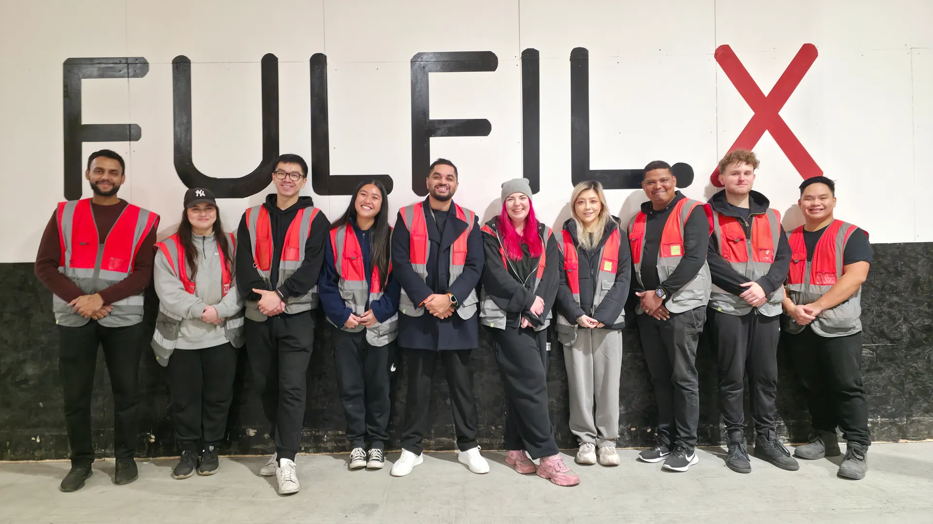 The FULFIL.X team standing together in front of the branded FULFIL.X warehouse wall